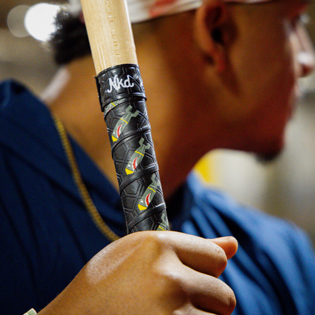 Photo of the bombs away bat grip wrapped around a wooden bat being held by someone waiting to hit a baseball.
