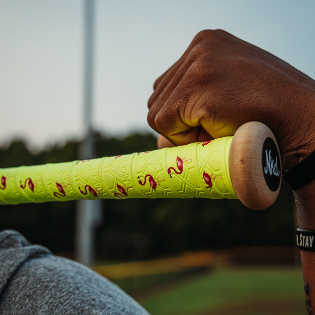 Photo of a wooden bat that is wrapped in the flamingo bat grip being held over a guys shoulder.