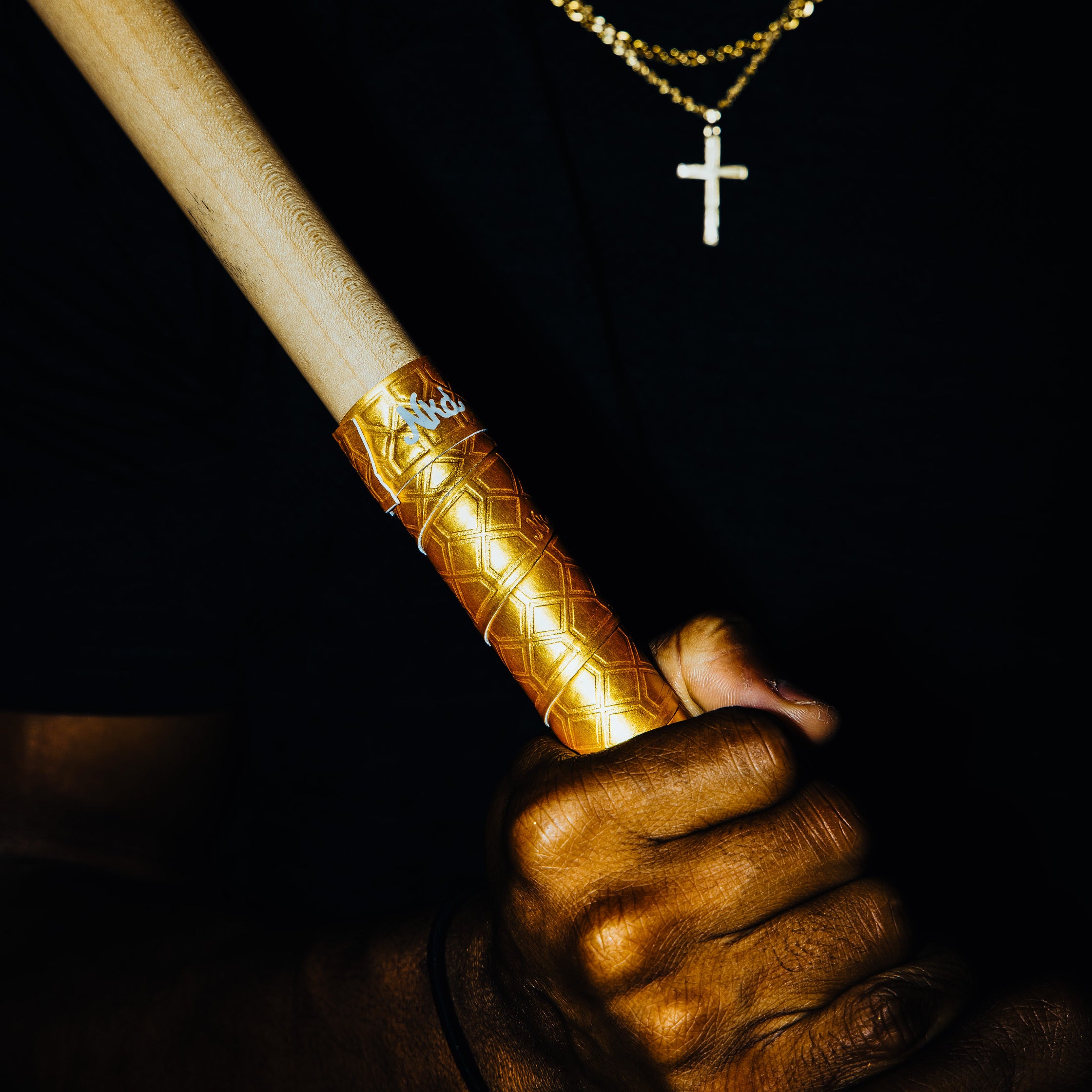 Photo of the golden bat grip being held at a slight angle in front of person torso on a black background.