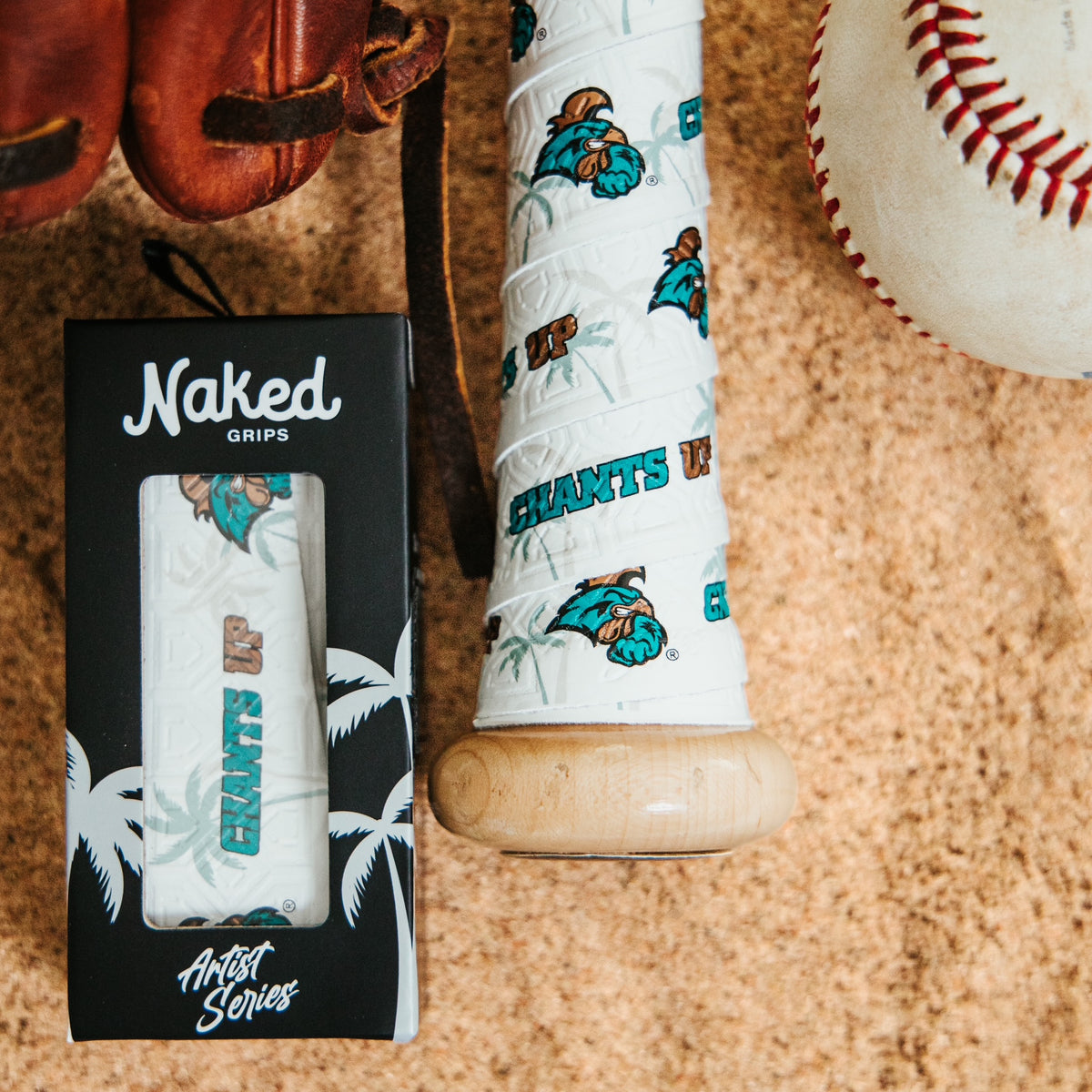 Coastal Carolina University themed bat grip with Chants Up text. Photo features bottom of bat handle wrapped with white grip with Chants. Up and the Coastal Carolina Chant logo along with a grip in a black artist series box, a baseball, and a glove all on beach sand.