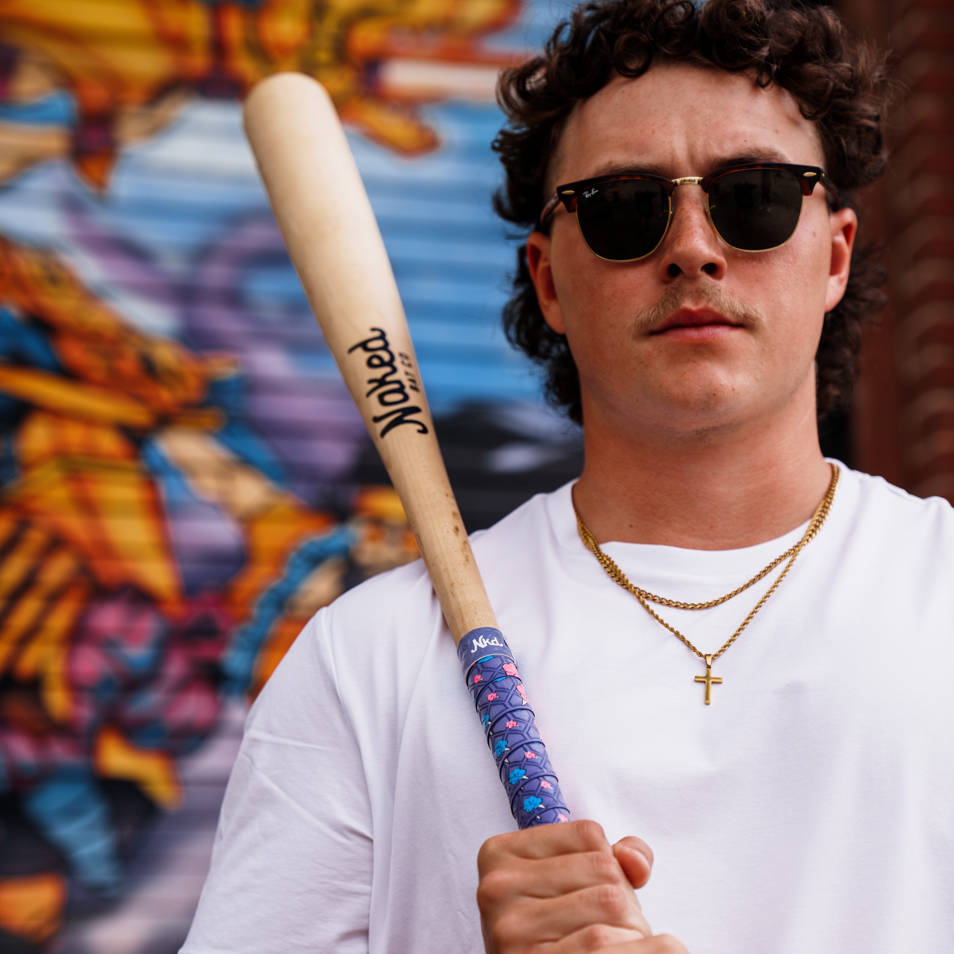 Photo of a man in sunglasses and white shirt holding a wooden bat wrapped with the cotton candy bat grip