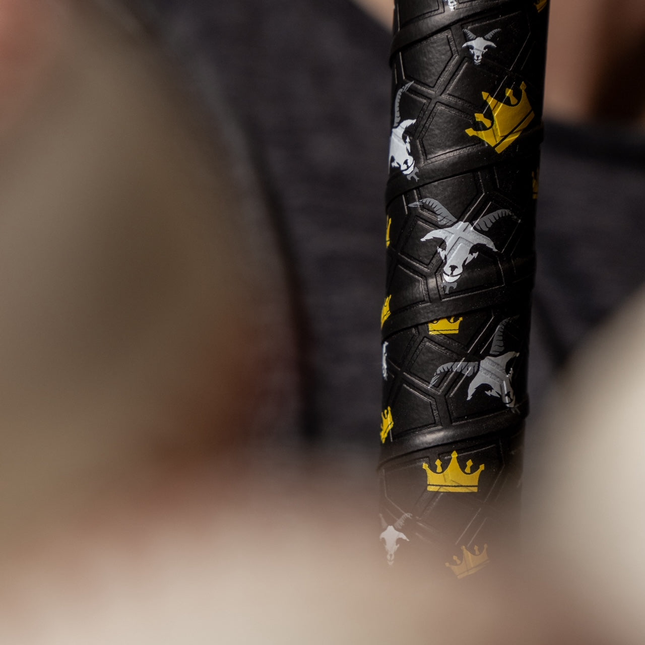 Photo of the goat bat grip wrapped around a wooden bat with baseballs out of focus in the foreground