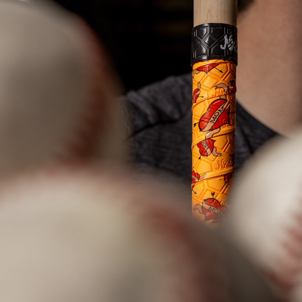 Image of the Mom bat grip wrapped on a wooden bat with baseballs in the foreground out of focus. 