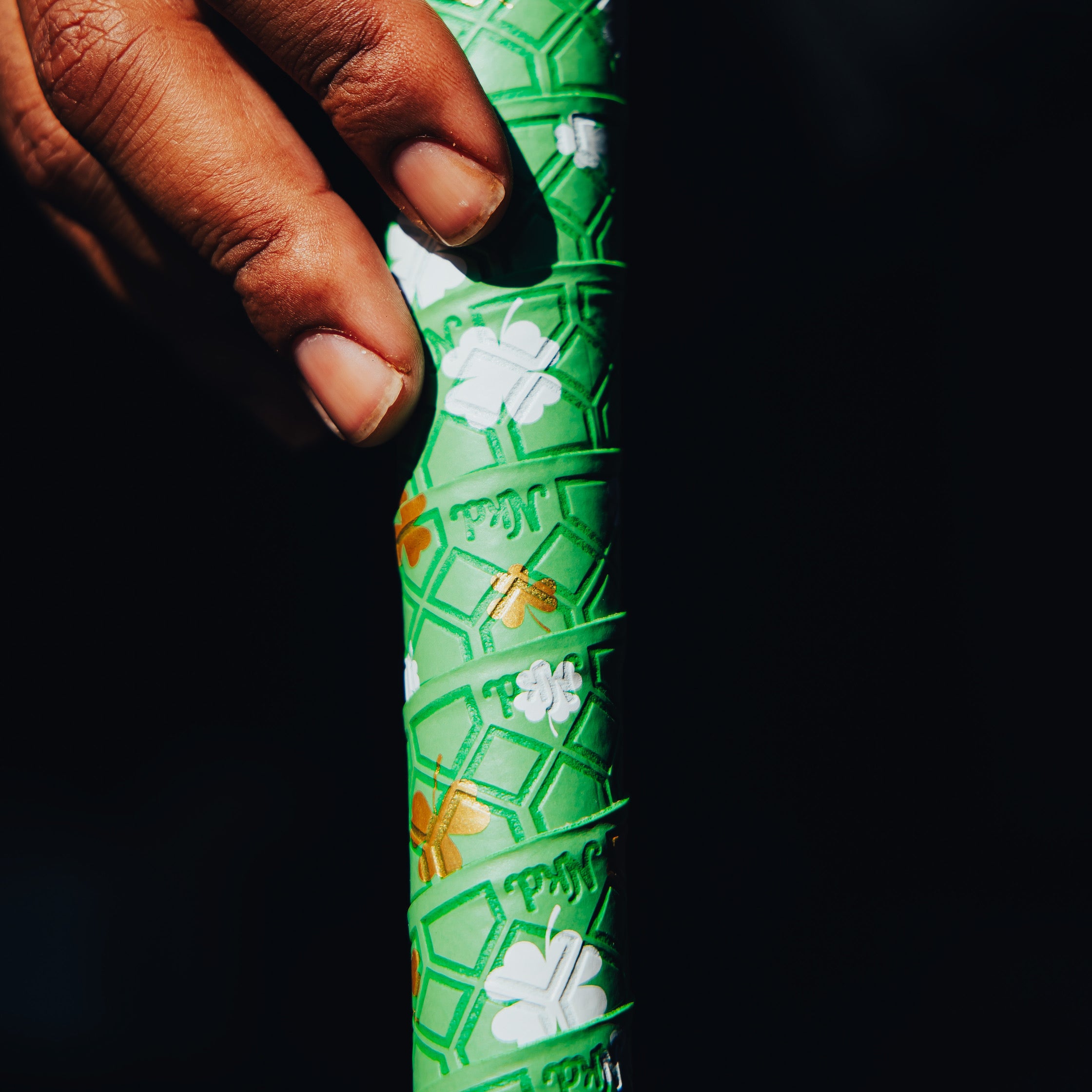 Photo of a baseball bat wrapped with the shamrock bat grip being held vertically with a hand holding the top left corder 