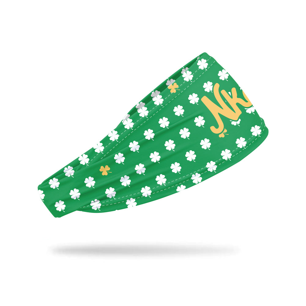 Photo of a green headband decorated with a white and gold shamrock pattern floating on a white background. 