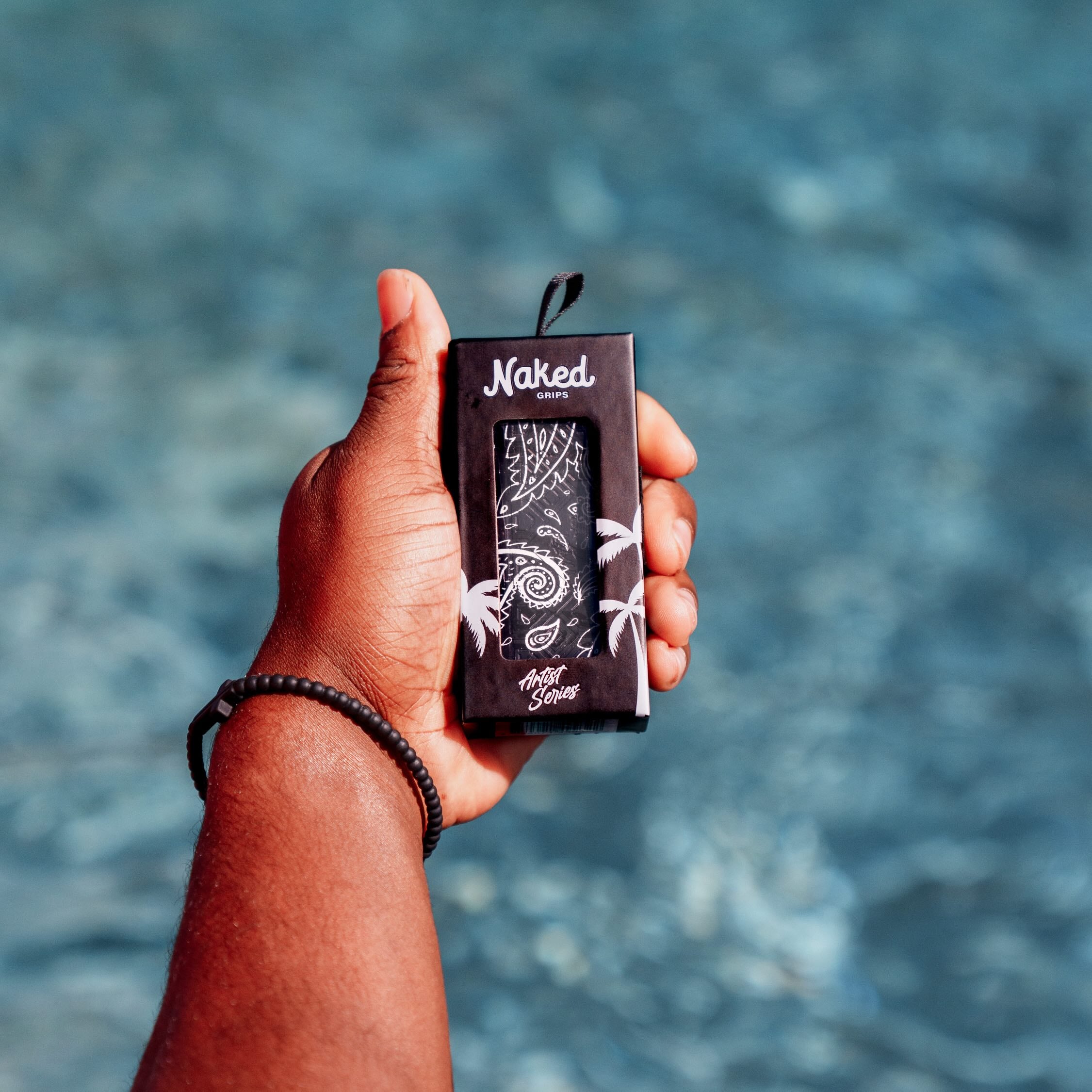 Photo of the black paisley bat grip being held in a left hand over a pool in the background. 
