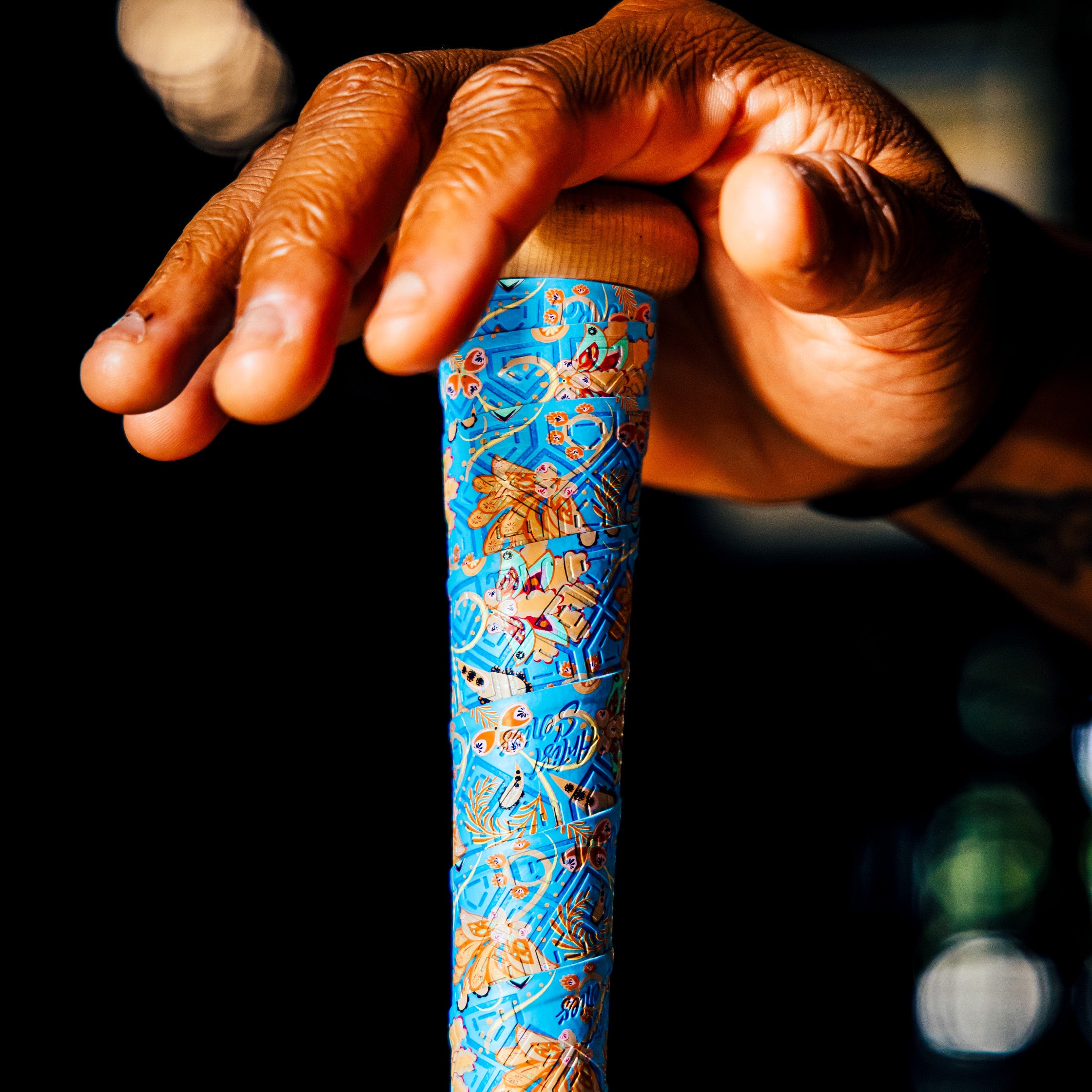 Photo of a wooden bat wrapped with the paisley bat grip with a hand holding it upright.