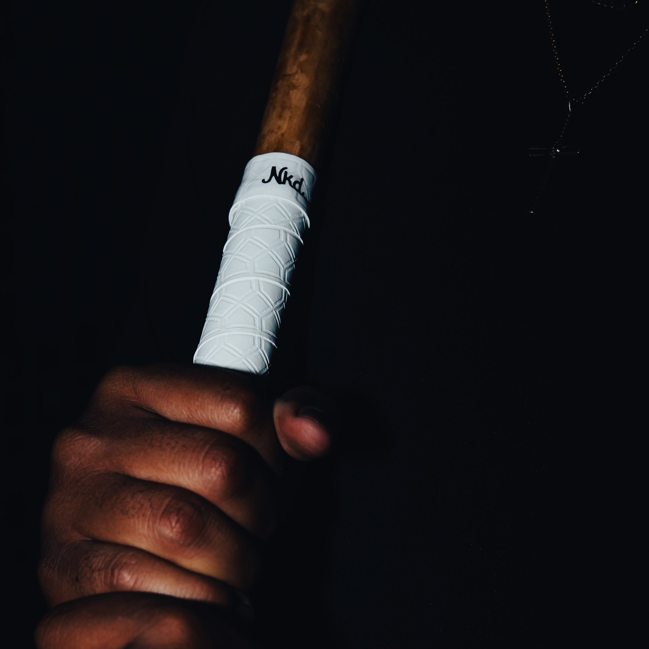 Photo of the white bat grip being held upright against a mans chest wearing a black shirt